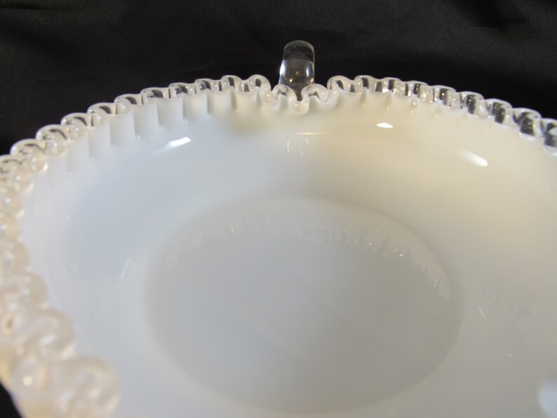 May include: White milk glass bowl with a silver rim and a clear glass handle. The bowl has a scalloped edge and a smooth, white interior.