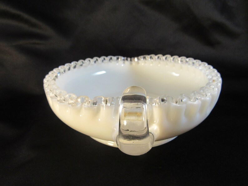 May include: A white milk glass bowl with a clear glass handle and a beaded rim. The bowl is a vintage style and has a scalloped edge.