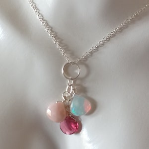 May include: A silver chain necklace with a charm featuring three gemstones: a pink opal, a blue opal, and a pink ruby.