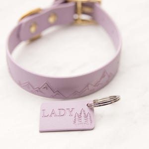 Può includere: Un collare per cani in pelle lavanda con un design a catena montuosa e un ciondolo per cani in pelle lavanda abbinato con la parola "LADY" e un design ad albero.