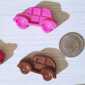 Puede incluir: Cuatro coches de juguete hechos de cera, en rosa, marr&oacute;n, rojo y verde. Los coches est&aacute;n dispuestos sobre una superficie de madera blanca. Tambi&eacute;n hay una moneda de veinticinco centavos de d&oacute;lar estadounidense de plata sobre la superficie.
