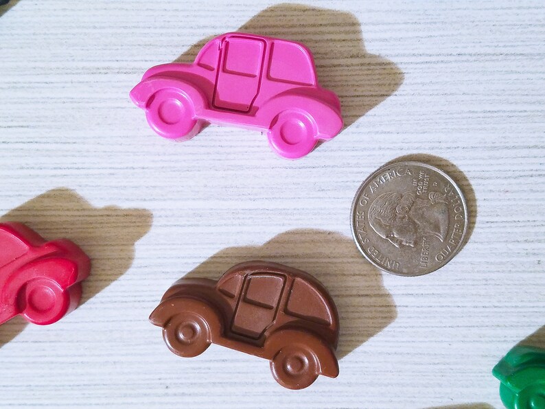 Puede incluir: Cuatro coches de juguete hechos de cera, en rosa, marr&oacute;n, rojo y verde. Los coches est&aacute;n dispuestos sobre una superficie de madera blanca. Tambi&eacute;n hay una moneda de veinticinco centavos de d&oacute;lar estadounidense de plata sobre la superficie.