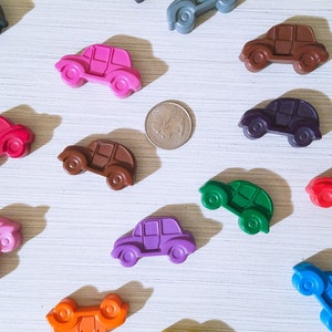 Puede incluir: Una colecci&oacute;n de 12 coches de juguete coloridos hechos de cera. Los coches son de varios colores, incluyendo rojo, verde, azul, morado, rosa, marr&oacute;n y negro. Los coches est&aacute;n dispuestos en un patr&oacute;n aleatorio sobre una superficie blanca.