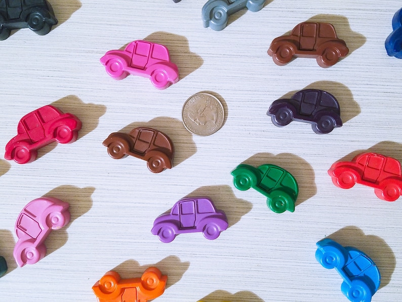 Puede incluir: Una colecci&oacute;n de 12 coches de juguete coloridos hechos de cera. Los coches son de varios colores, incluyendo rojo, verde, azul, morado, rosa, marr&oacute;n y negro. Los coches est&aacute;n dispuestos en un patr&oacute;n aleatorio sobre una superficie blanca.