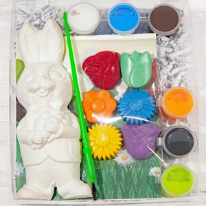 May include: A paint-your-own ceramic Easter bunny kit with a green paintbrush, six paint pots, and five ceramic flower shapes. The bunny is holding a flower.