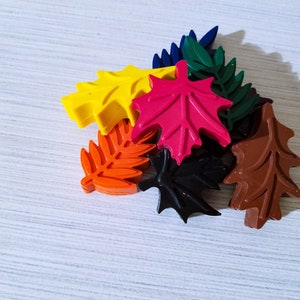 May include: A set of seven colorful wax leaf shapes, including red, yellow, orange, brown, black, and green. The leaves are arranged in a pile on a white surface.
