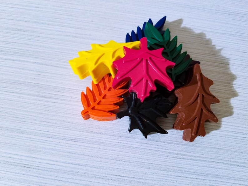 May include: A set of seven colorful wax leaf shapes, including red, yellow, orange, brown, black, and green. The leaves are arranged in a pile on a white surface.