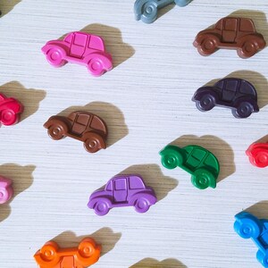 Puede incluir: Una colecci&oacute;n de 12 coches de juguete coloridos hechos de cera. Los coches son de varios colores, incluyendo rojo, azul, verde, morado, naranja, marr&oacute;n, rosa y negro. Los coches est&aacute;n dispuestos en un patr&oacute;n sobre una superficie blanca.