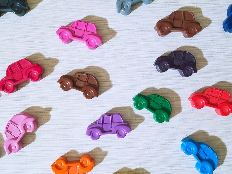 Puede incluir: Una colecci&oacute;n de 12 coches de juguete coloridos hechos de cera. Los coches son de varios colores, incluyendo rojo, azul, verde, morado, naranja, marr&oacute;n, rosa y negro. Los coches est&aacute;n dispuestos en un patr&oacute;n sobre una superficie blanca.