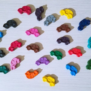 Puede incluir: Una colecci&oacute;n de 20 peque&ntilde;os coches de juguete de colores hechos de cera. Los coches est&aacute;n dispuestos en forma de semic&iacute;rculo sobre una superficie blanca. Los coches son de diferentes colores, incluyendo rojo, azul, verde, amarillo, naranja, morado, rosa y negro.