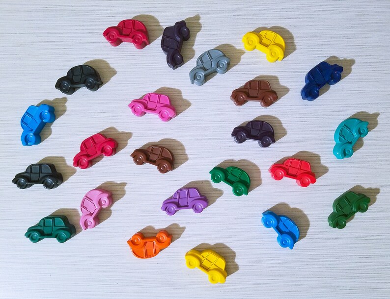 Puede incluir: Una colecci&oacute;n de 20 peque&ntilde;os coches de juguete de colores hechos de cera. Los coches est&aacute;n dispuestos en forma de semic&iacute;rculo sobre una superficie blanca. Los coches son de diferentes colores, incluyendo rojo, azul, verde, amarillo, naranja, morado, rosa y negro.