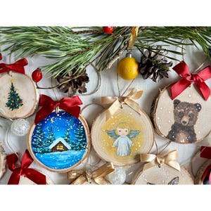 May include: A set of eight wooden Christmas ornaments with hand-painted designs. The ornaments feature a winter scene with a house, a Christmas tree, an angel, a bear, and other designs. The ornaments are decorated with red, gold, and white ribbons.