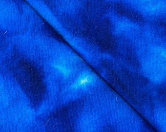 May include: Close-up of a vibrant blue fabric with a tie-dye pattern. The fabric is folded diagonally, creating a contrast of light and dark blue hues. The texture appears soft and possibly made of cotton or a similar material.