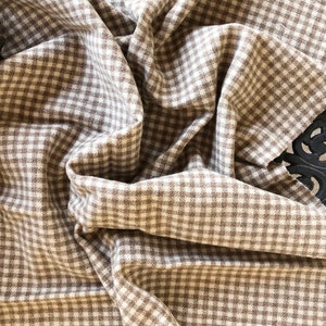 May include: A brown and white gingham fabric with a woven texture. The fabric is folded and draped.