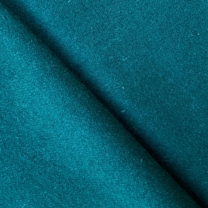 May include: Close-up of a folded piece of teal fabric. The fabric has a soft, textured appearance with subtle variations in color. The folds create shadows and depth, highlighting the material's texture and color.