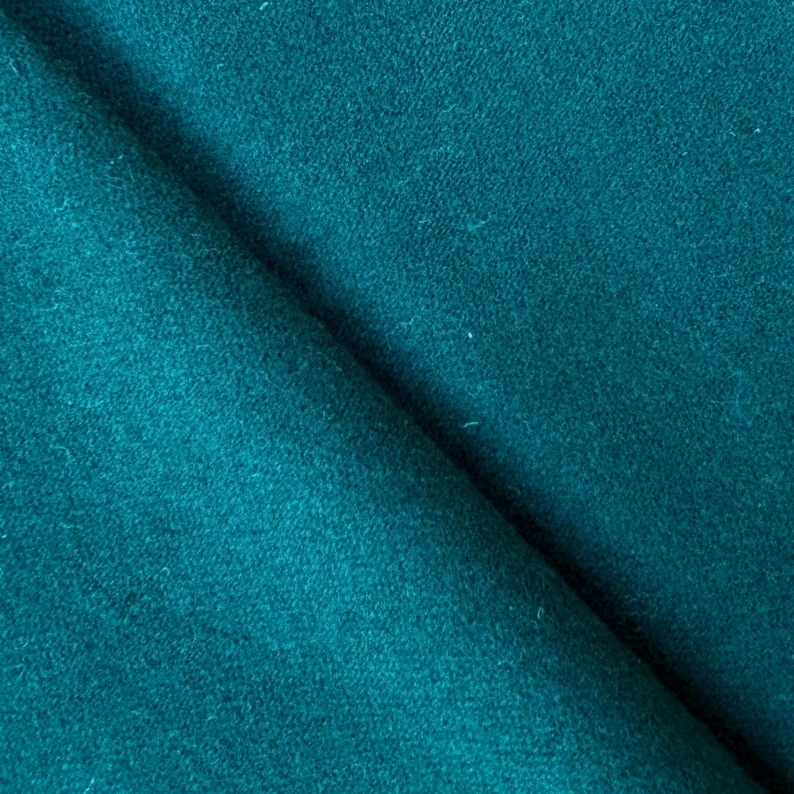 May include: Close-up of a folded piece of teal fabric. The fabric has a soft, textured appearance with subtle variations in color. The folds create shadows and depth, highlighting the material's texture and color.