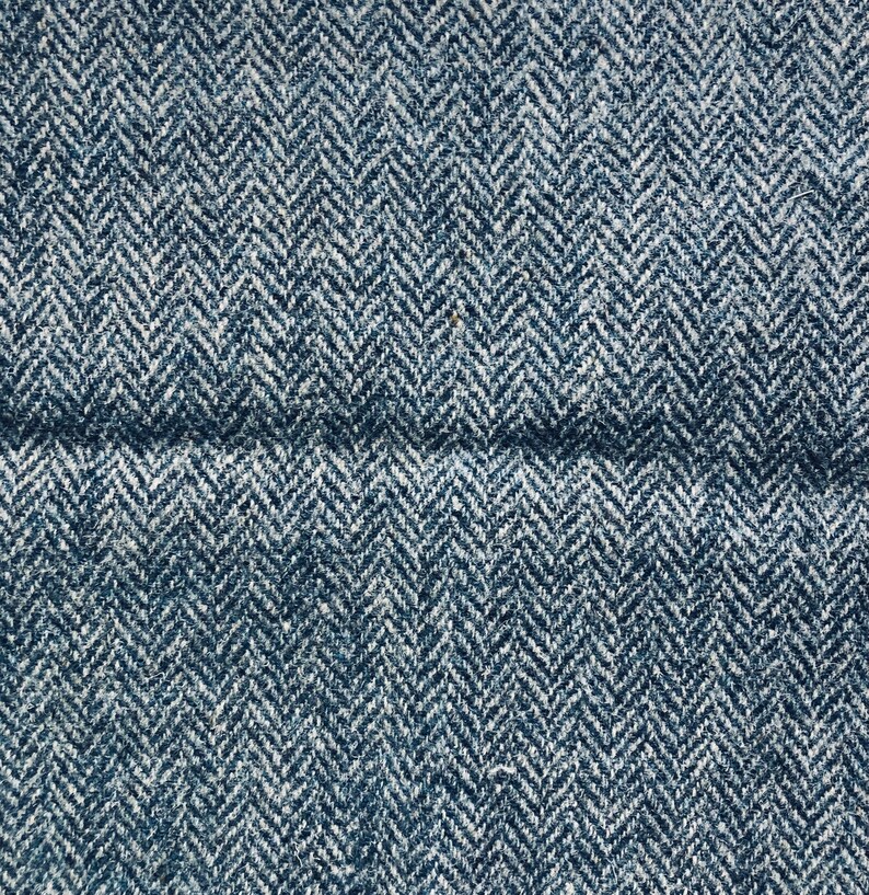 May include: Close-up of a blue and white herringbone fabric. The fabric has a subtle texture and a woven pattern.