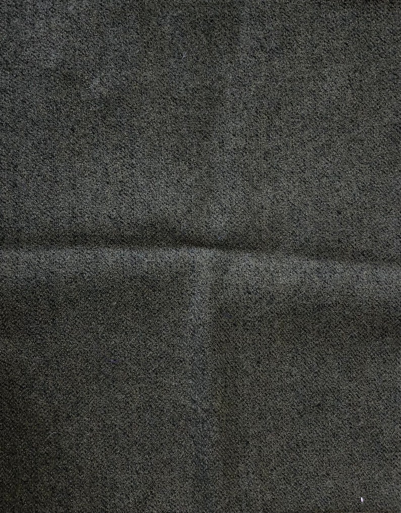 Pu&ograve; includere: Primo piano di un tessuto di colore grigio scuro con una texture e una piega sottile al centro.
