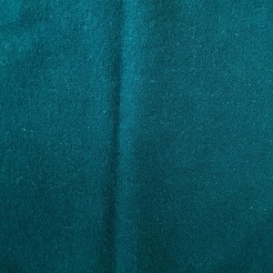 May include: Close-up of a teal fabric with a soft, textured surface. The fabric has subtle variations in color and a slight sheen, suggesting a high-quality material. The folds and creases add depth to the image.