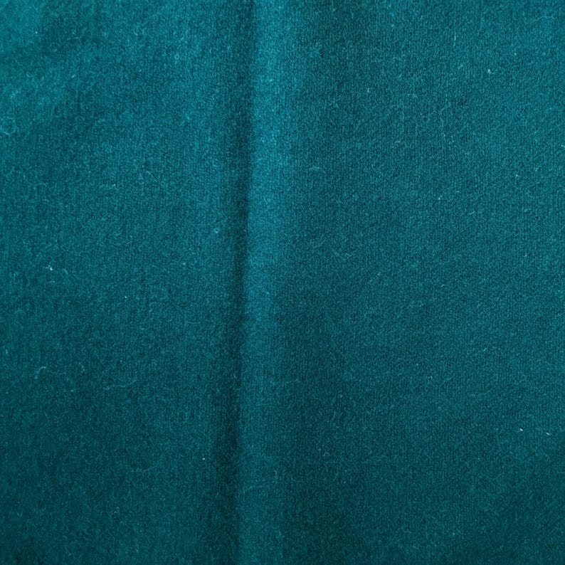 May include: Close-up of a teal fabric with a soft, textured surface. The fabric has subtle variations in color and a slight sheen, suggesting a high-quality material. The folds and creases add depth to the image.