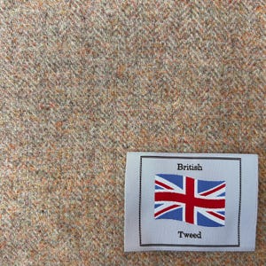 May include: A close-up of a beige tweed fabric with a white label that reads "British Tweed" and features a red, white, and blue Union Jack flag.