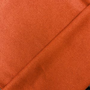 May include: Close-up of a rust-colored fabric with a smooth, even texture. The fabric is folded in half, creating a diagonal line across the image.