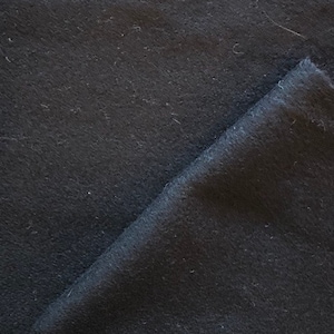 Puede incluir: Primer plano de una tela gris oscuro con una superficie texturizada. La tela est&aacute; doblada por la mitad, mostrando el interior de la tela.