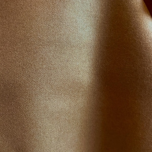 May include: A close-up of a brown fabric with a subtle sheen. The fabric has a soft, textured surface.