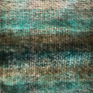 May include: Close-up of a woven textile with a textured, fuzzy surface. The color palette includes shades of teal, brown, and pink, creating a striped pattern. The weave is visible, adding to the tactile appearance of the fabric.