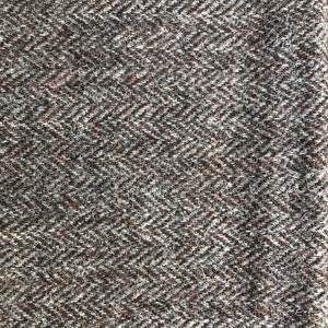 May include: Close-up of a brown and white herringbone tweed fabric. The fabric has a textured surface and a subtle sheen.