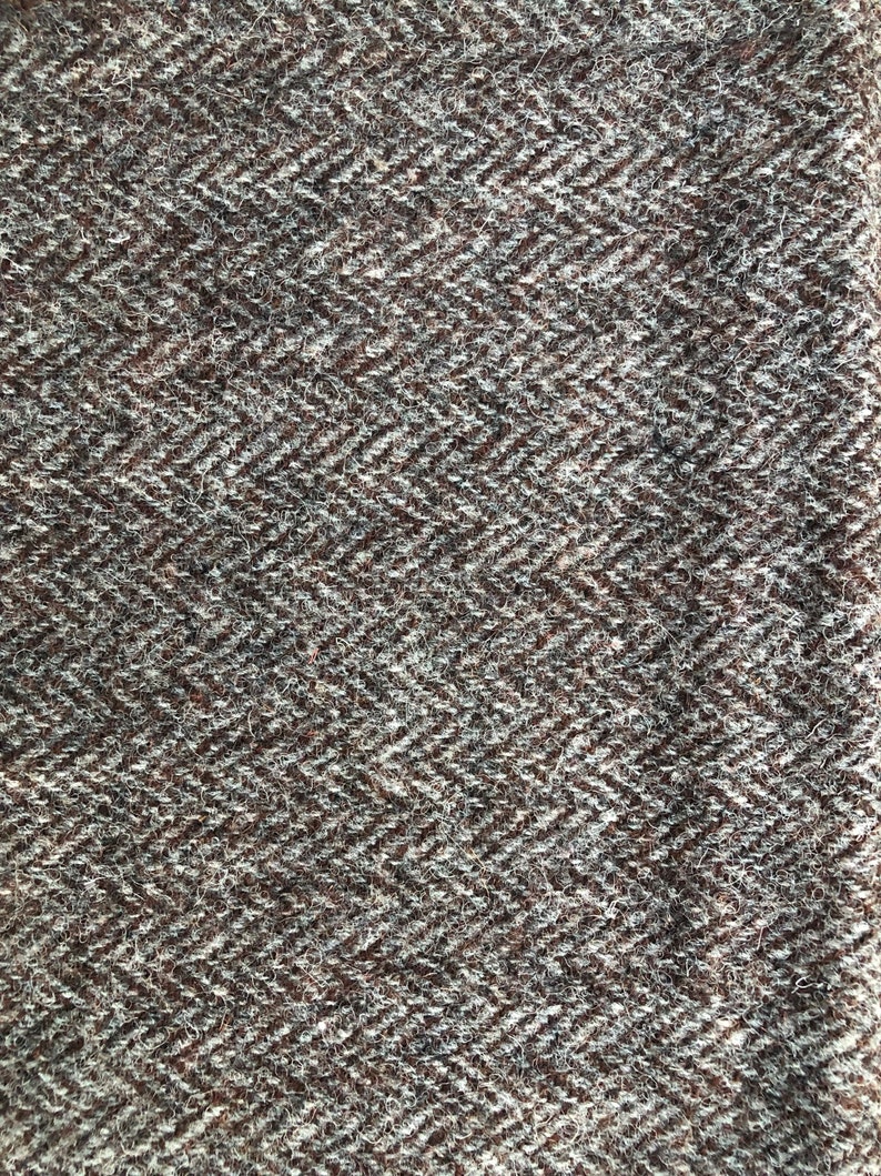 May include: Close-up of a brown and white herringbone tweed fabric. The fabric has a textured surface and a subtle sheen.