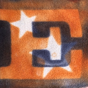 May include: A close-up of a brown and orange fabric with a dark blue letter "E" outlined in white stars. The fabric has a fuzzy texture.