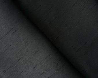 May include: A close-up shot of black fabric with a subtle sheen. The material is folded, revealing the texture and direction of the weave. The dark color and slight sheen suggest a luxurious textile, possibly silk or a similar material.
