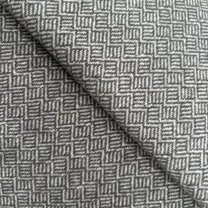 May include: Close-up of a folded fabric with a geometric pattern. The fabric features a repeating design of gray and white squares and rectangles, creating a textured appearance. The material appears to be woven, with a slight sheen.
