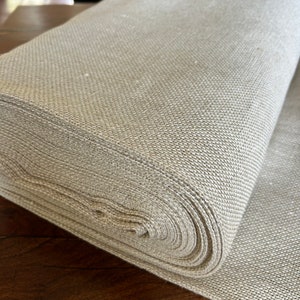 May include: A roll of natural linen fabric, tightly wound and showing the texture of the woven material.