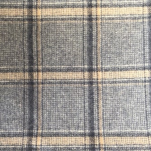 Pu&ograve; includere: Primo piano di un tessuto a quadri grigio e beige. Il tessuto ha una trama intrecciata con un motivo di linee intersecanti in grigio, beige e grigio scuro, creando un classico disegno a quadri. Il tessuto sembra essere un materiale di peso medio.