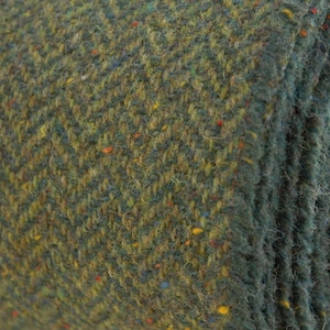 May include: Close-up of a green tweed fabric with a herringbone pattern. The fabric has a subtle texture and is woven with multi-colored threads, including yellow, blue, and red.