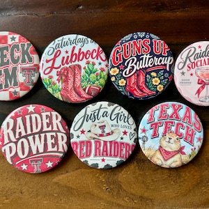 May include: Seven circular pin-back buttons featuring Texas Tech themes. Designs include text such as Wreck 'Em, Saturdays in Lubbock, Guns Up Buttercup, Raiderland Social Club, Raider Power, Just a Girl Who Loves Red Raiders, and Texas Tech with a prairie dog.
