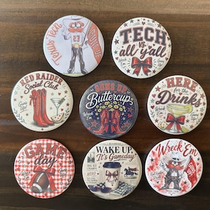 May include: Eight circular pinback buttons featuring Texas Tech University themes. Designs include a mascot, red cowboy boots, a football, a coffee cup, and text such as "Tech vs. all y'all," "Red Raider Social Club," "Guns Up," and "Wreck 'Em."