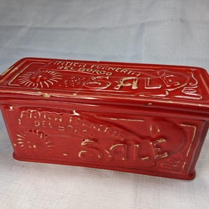 Puede incluir: Un recipiente rectangular de cer&aacute;mica roja con tapa. El recipiente tiene texto en relieve que dice "ANTICA FORNERIA DEL BORGO SALE". La palabra "SALE" es prominente. El dise&ntilde;o incluye motivos de rayos de sol y florales.