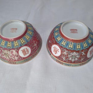 May include: Two decorative ceramic bowls with a red, blue, and yellow floral design. Each bowl features a white interior and a repeating Chinese character in a white circle. The bowls are likely for serving or display.