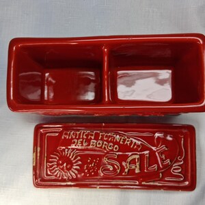Puede incluir: Un recipiente rectangular de cer&aacute;mica roja, dividido en dos secciones, con tapa a juego. La tapa presenta el texto "ANTICA FORNERIA DEL BORGO SALE" y un dise&ntilde;o de sol. Para cocina o decoraci&oacute;n del hogar.