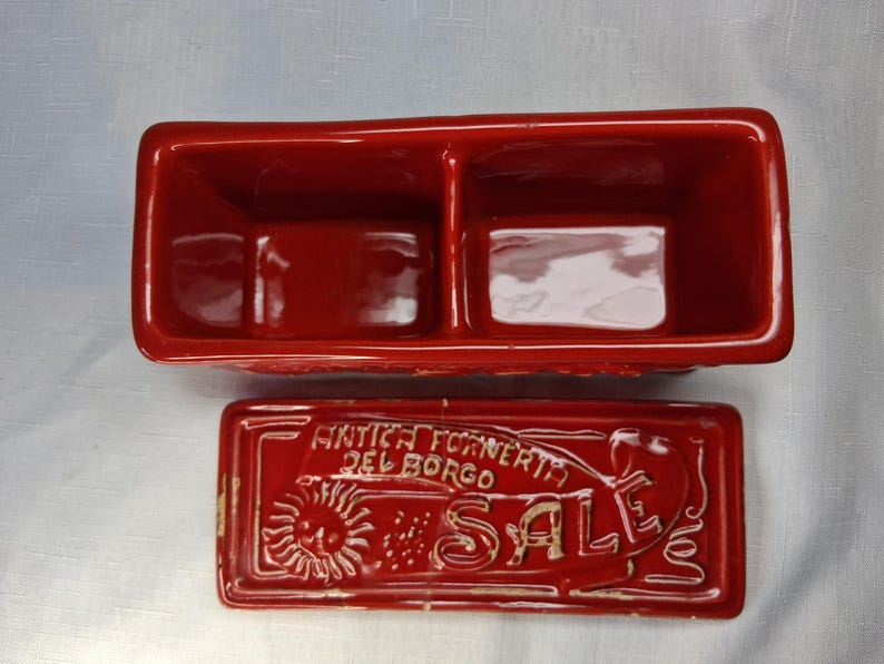 Puede incluir: Un recipiente rectangular de cer&aacute;mica roja, dividido en dos secciones, con tapa a juego. La tapa presenta el texto "ANTICA FORNERIA DEL BORGO SALE" y un dise&ntilde;o de sol. Para cocina o decoraci&oacute;n del hogar.