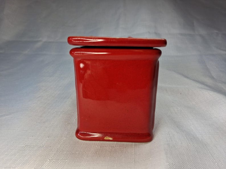 Puede incluir: Un peque&ntilde;o recipiente rectangular de cer&aacute;mica roja con tapa a juego. El recipiente tiene un acabado brillante y una base ligeramente redondeada. La tapa encaja a ras. Para almacenamiento o exhibici&oacute;n.