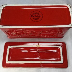 Puede incluir: Una mantequera rectangular de cer&aacute;mica roja con tapa a juego. El plato tiene un borde blanco y detalles en relieve. La tapa est&aacute; separada, mostrando el interior. Ideal para uso en la cocina.