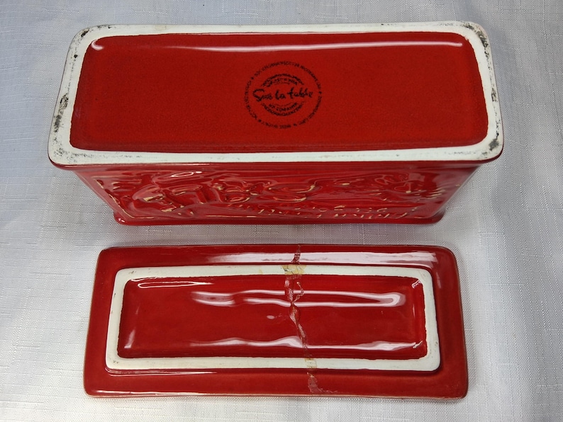 Puede incluir: Una mantequera rectangular de cer&aacute;mica roja con tapa a juego. El plato tiene un borde blanco y detalles en relieve. La tapa est&aacute; separada, mostrando el interior. Ideal para uso en la cocina.