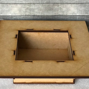Puede incluir: Una caja de madera con una abertura cuadrada en la parte superior. La caja est&aacute; hecha de madera marr&oacute;n claro y tiene un borde marr&oacute;n oscuro.