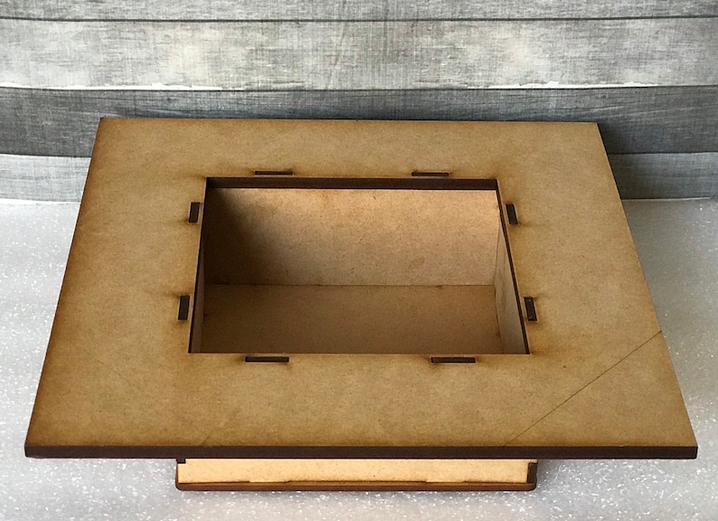 Puede incluir: Una caja de madera con una abertura cuadrada en la parte superior. La caja est&aacute; hecha de madera marr&oacute;n claro y tiene un borde marr&oacute;n oscuro.