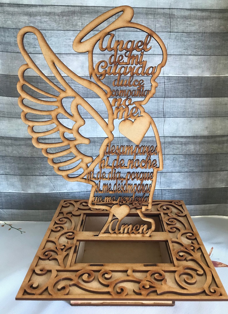 Puede incluir: Corte de madera de un &aacute;ngel con alas, halo y coraz&oacute;n. El &aacute;ngel sostiene un rollo con el texto "Angel de mi Guarda dulce compania no me desampares ni de noche ni de dia porque si me desamparas yo me perderia Amen".