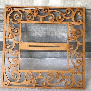 Puede incluir: Un marco de madera con un dise&ntilde;o decorativo e intrincado. El marco tiene un recorte en el centro, creando un espacio para una imagen u otro elemento decorativo.